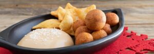 Plato tradicional colombiano con porción de natilla espolvoreada con coco, buñuelos dorados y hojuelas en una cazuela negra.