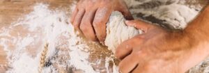 Manos de un panadero amasando una masa para pan sobre una mesa de madera cubierta de harina.