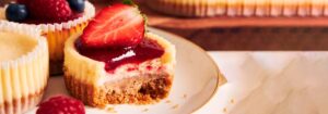 Mini cheesecake con mermelada de frutos rojos y una fresa fresca encima, con un mordisco que muestra su textura interna.