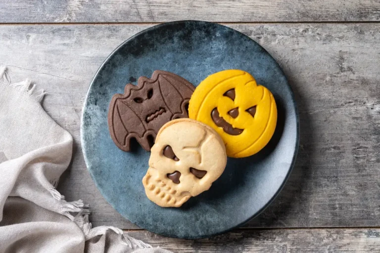Tres galletas de Halloween con relleno de chocolate (un murciélago, una calabaza y una calavera) en un plato azul sobre madera.